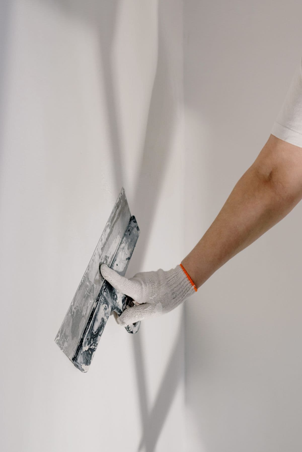 Gloved hand smoothing joint compound on a wall with a taping knife
