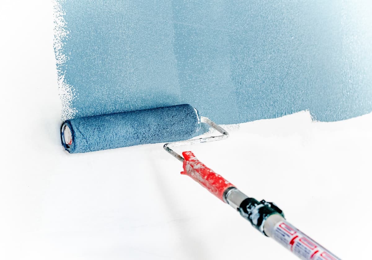 Paint roller applying blue paint to a white wall